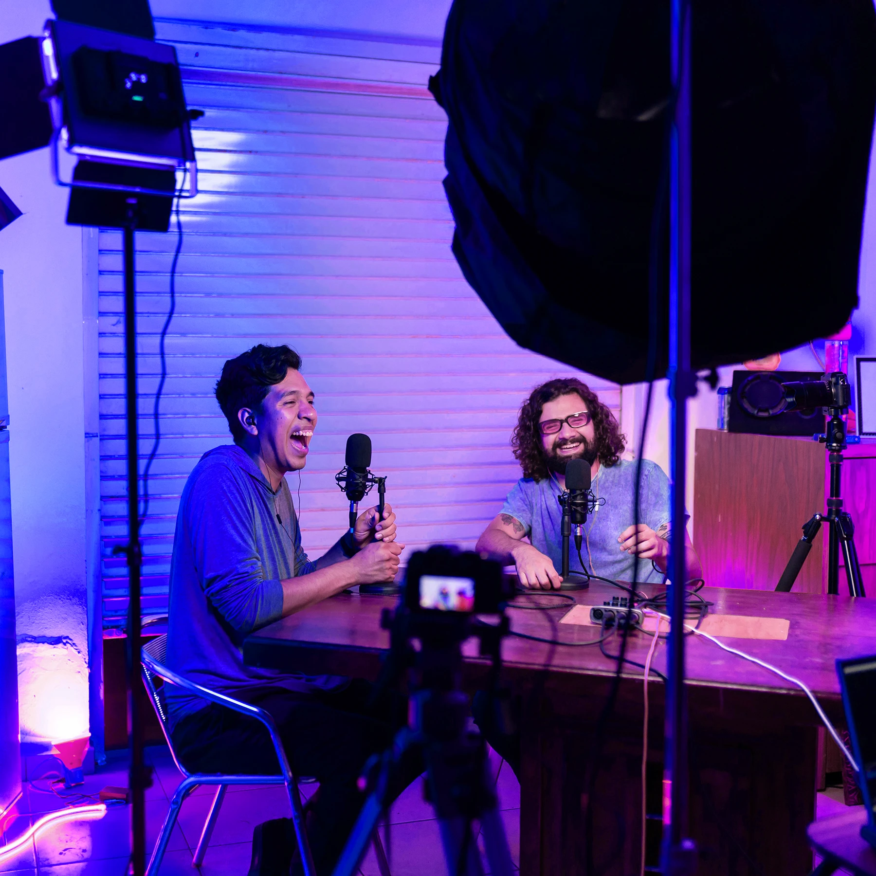 An image of a video shoot with two men talking and smiling in front of lighting gear.